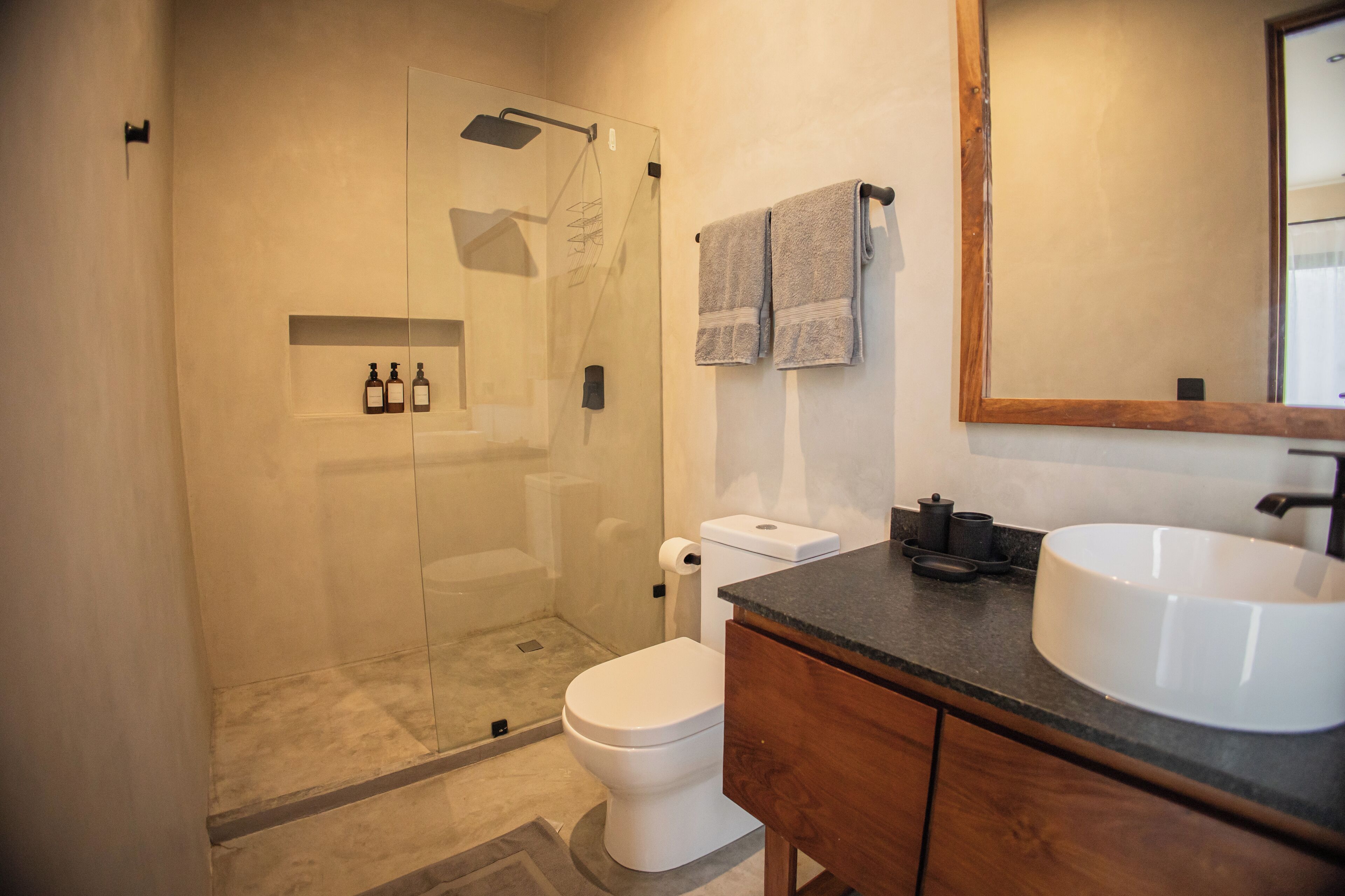 A modern bathroom with a glass-enclosed shower, a white toilet, a wooden vanity with a large sink, and a mirror.