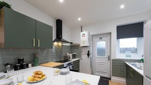 A modern kitchen with grey cabinets, a microwave, a stove, and a dining area set with plates and glasses. - Luke Stays - Grace Street (Tyne and Wear)
