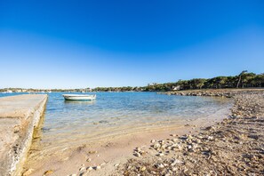 A beach with a boat, clear water, and a rocky shoreline. - Villa Lucia in Portocolom: Seafront House with Garden, BBQ & Air Conditioning (Portocolom)