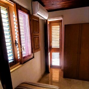 A room with a wooden door, a window with blinds, and an air conditioning unit mounted on the wall. - Grandma Maria's House - Maestrale (Scilla)