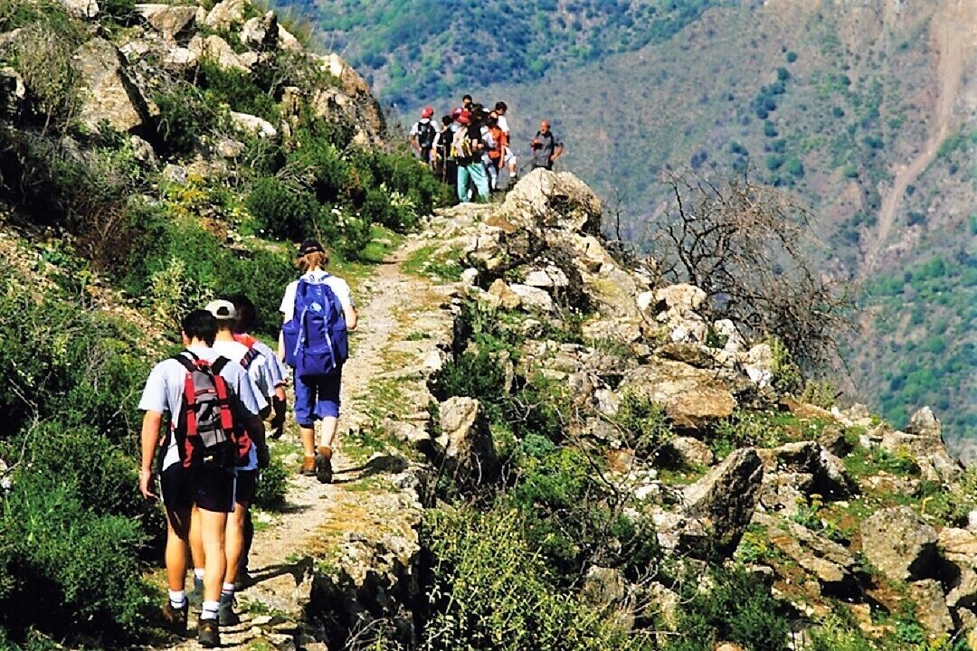 A group of hikers on a rocky mountain trail with a view of the valley below.