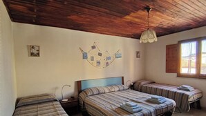 Ein Zimmer mit drei Betten, einer Holzbalkendecke, einer wandmontierten Leuchte und einem Fenster mit Vorhängen.