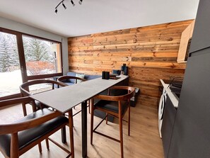 Ett modernt kök med träpanel, en matplats med ett långt bord och stolar, och utsikt över ett snötäckt landskap genom stora fönster.