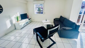 Un salon moderne avec un canapé, un téléviseur, une petite table et un fauteuil.