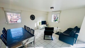 Un salon comprenant une table à manger, des chaises, un canapé, un téléviseur et une horloge murale.