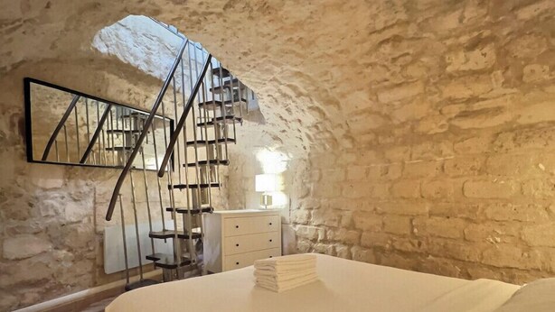Un dormitorio con cama, cómoda, espejo y una escalera de caracol frente a una pared de piedra.