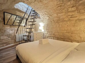 Ein Schlafzimmer mit einem Bett, einem Schminktisch, einem Spiegel und einer Wendeltreppe an einer Steinwand.