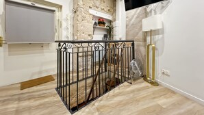 Un interior moderno con una escalera, un televisor de pantalla plana montado en la pared y un estante pequeño con objetos decorativos.