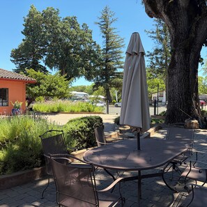 Une terrasse extérieure avec une table et des chaises, entourée de verdure et d’arbres.
