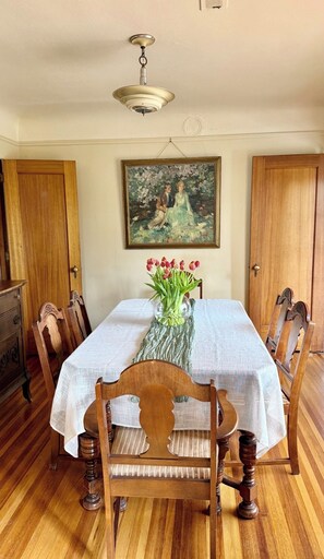 Een eetkamer met een tafel gedekt voor vier personen, houten stoelen, een vaas met tulpen en een schilderij aan de muur.