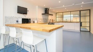 Una cocina moderna con encimera de madera, taburetes de bar blancos, microondas y un televisor fijado a la pared.