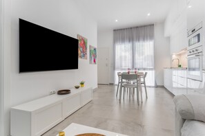 Una sala moderna con televisor de pantalla plana, un comedor con mesa y sillas, y una kitchenette con armarios y electrodomésticos.