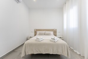 A minimalist hotel room with a bed, two bedside tables, a wooden headboard, and a large window with curtains. - Apartment 'Arena Suite Fuengirola' with Wi-Fi and Air Conditioning (Fuengirola)
