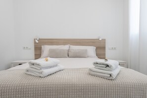 A neatly made bed with a textured blanket, two folded towels on the bed, and a wooden headboard. - Apartment 'Arena Suite Fuengirola' with Wi-Fi and Air Conditioning (Fuengirola)