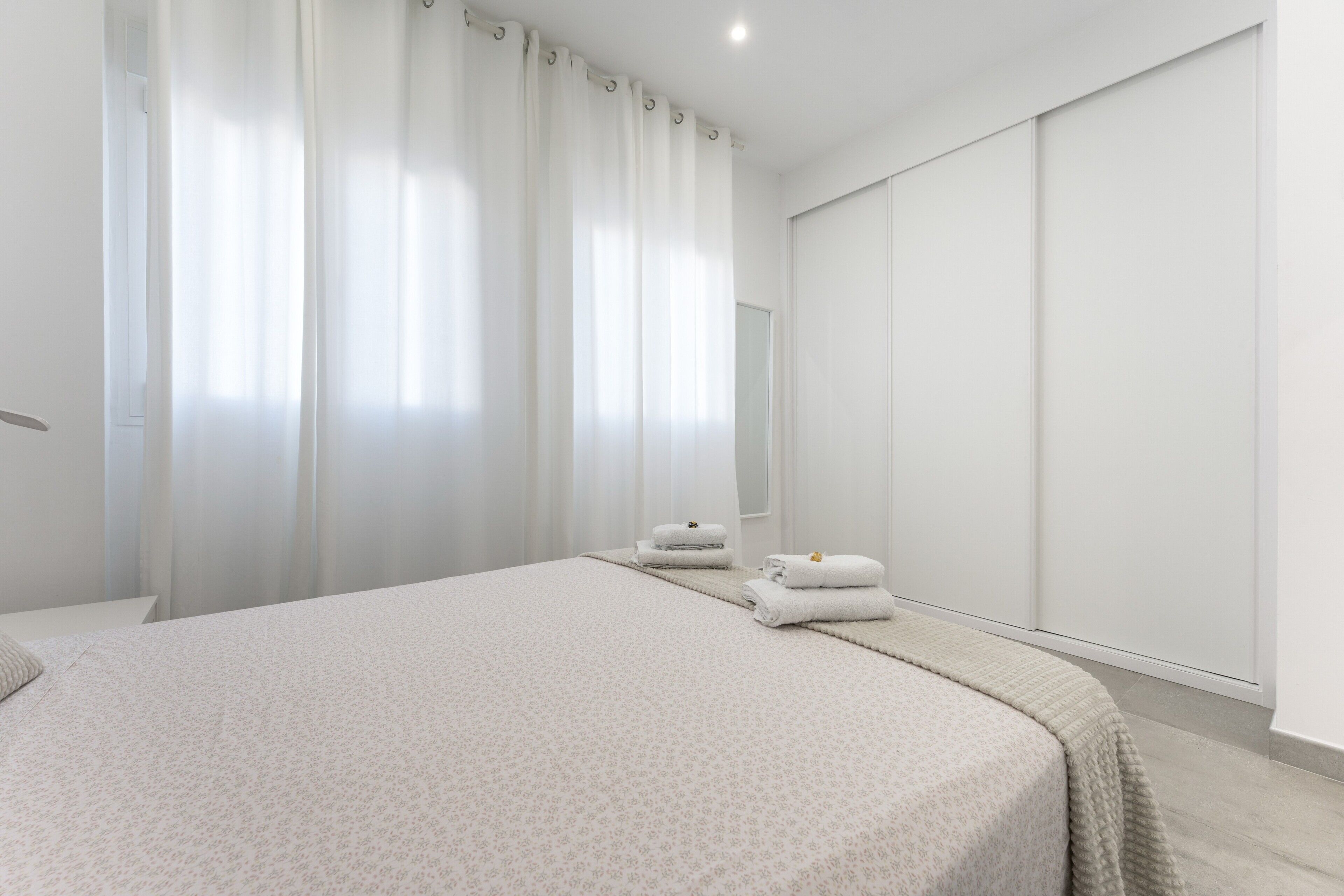 A bedroom with a large bed, a bedside table, a mirror, and a wardrobe.