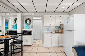Una cocina funcional con armarios blancos, un refrigerador blanco, microondas y un comedor con mesa y sillas.