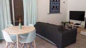 A living room with a sofa, a round table with chairs, a TV, and a wall-mounted artwork. - Villa Casa Kuito - Estoi (Estói)