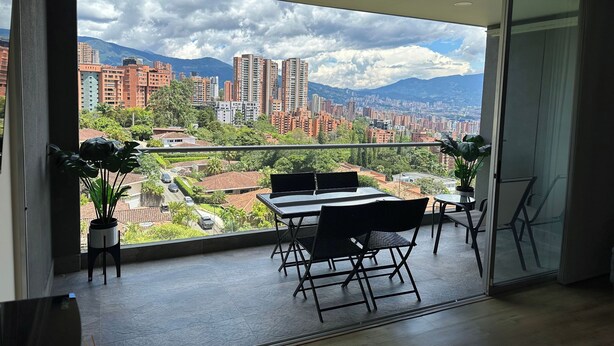 Un balcon avec vue sur la ville, une table à manger, des chaises et des plantes en pot.