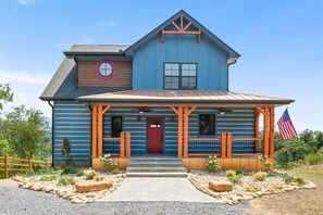 Ein zweistöckiges Haus mit roter Tür, einer Veranda mit Holzgeländern und einer amerikanischen Flagge.