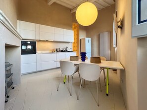 Kompakti keittiö, jossa on valkoiset kaapit, sisäänrakennettu uuni sekä ruokailutila, jossa on kaksi tuolia ja pöytä.