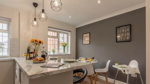 A modern kitchen with a marble island, pendant lights, and a dining area with chairs and a high chair. - 3BR Luxury Chic Spacious House w/Parking -Sleeps 7 (Southampton)