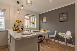 Une cuisine moderne dotée d’un îlot en marbre, de luminaires suspendus et d’un coin repas avec des chaises et une chaise haute.