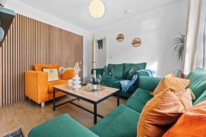 Ein modernes Wohnzimmer mit einer Wand aus Holzleisten, einem grünen Sofa, einem orangefarbenen Sessel und einem Couchtisch.