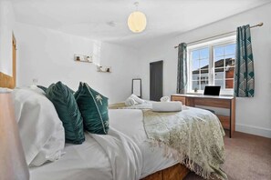 Een slaapkamer met een bed, een bureau, een raam met gordijnen, een radiator en een hanglamp.