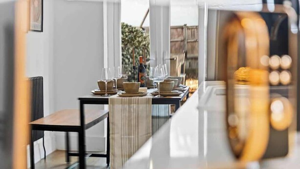 Un'area pranzo con un tavolo lungo apparecchiato per più persone, una bottiglia di vino e vista sull'esterno.