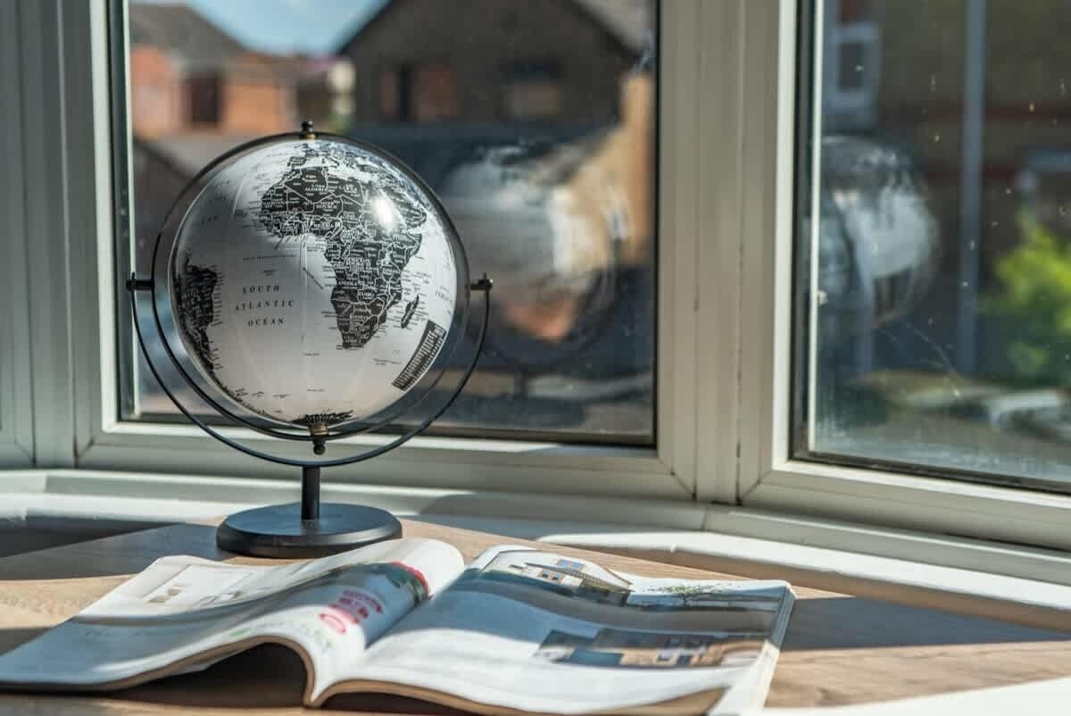 A globe on a stand next to an open magazine on a windowsill.