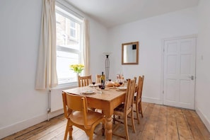 Ein Esszimmer mit Holztisch, Stühlen, einem Blumenstrauß und einem Spiegel an der Wand.
