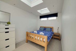A bedroom with a skylight, a bed with a blue patterned bedspread, a bedside table, and a white dresser.