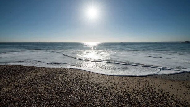 Ein Strand mit Kieselsteinen, Wellen und blauem Himmel.