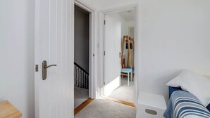 Ein Flur, der in ein Schlafzimmer mit einem Bett, einer hölzernen Bank und einer Tür mit Griff führt.