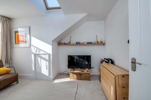 A modern living room with a TV, wooden furniture, a bookshelf, and a skylight.