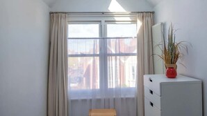 Ein Zimmer mit Oberlichtern, einem großen Fenster mit Vorhängen, einer hölzernen Bank und einem weißen Schrank mit Pflanze.