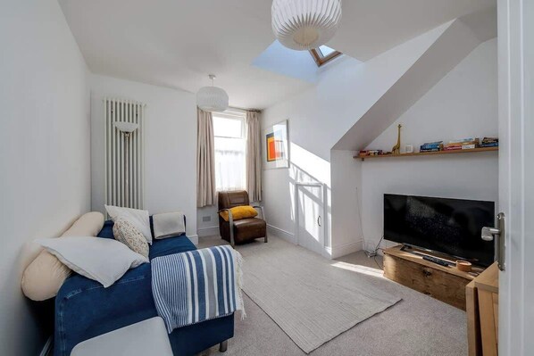 A modern living room with a bed, a TV, a chair, and a skylight.