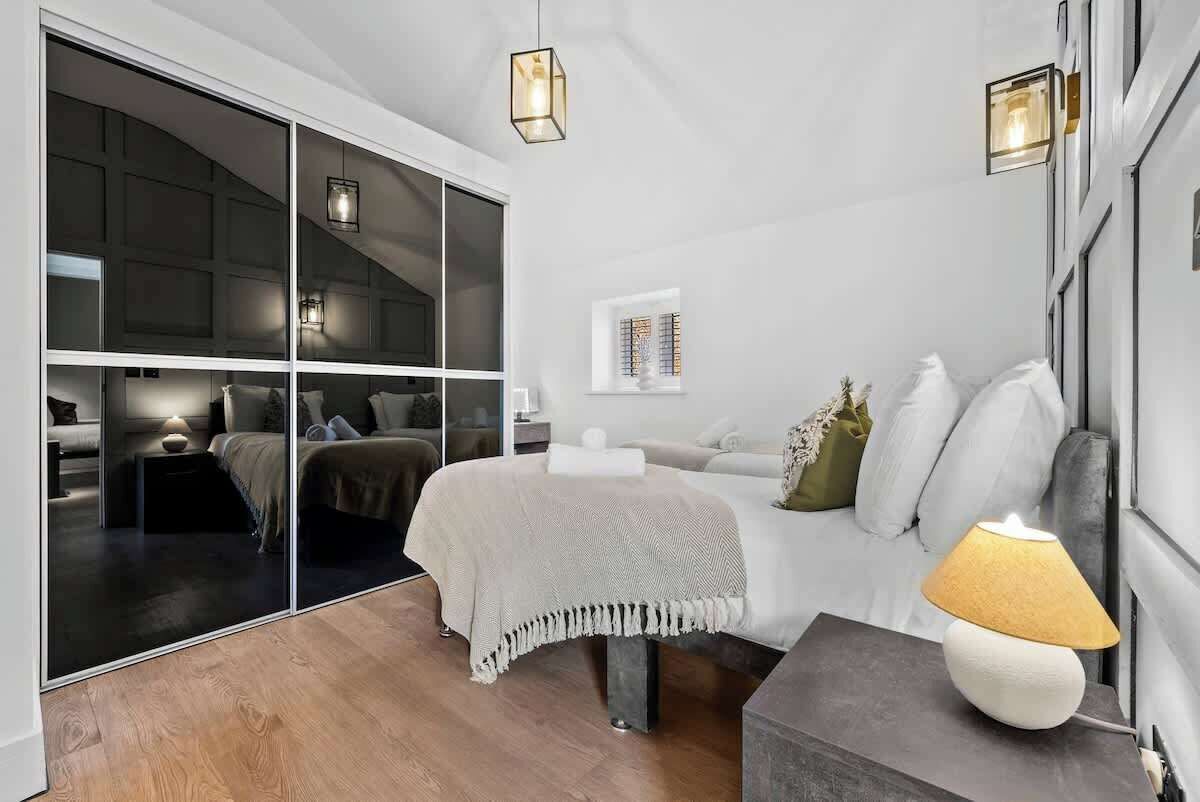 Une chambre à coucher moderne avec une grande porte coulissante, un lit recouvert d’un jeté blanc, une table de chevet et une lampe.