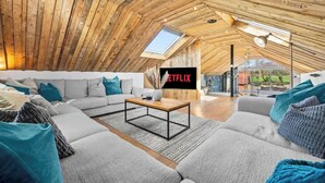 Ein moderner Loft-Wohnraum mit schrägverdachter Decke, einem großen Sofa, einem Couchtisch und einem Schild für Netflix.