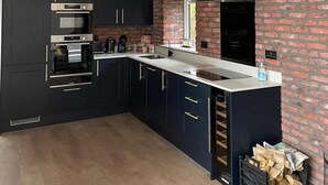 Une cuisine moderne avec des meubles de couleur sombre, un mur d’accent en briques, un îlot central et un luminaire suspendu.