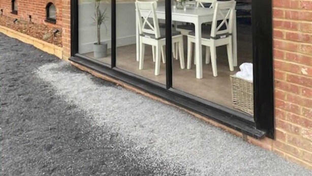 Un bâtiment moderne doté de grandes fenêtres en verre, d’une façade en briques et d’un espace extérieur aménagé avec des chaises blanches et une table.