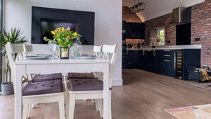 Une cuisine moderne avec un mur en briques, un coin repas avec une table et des chaises blanches, et un téléviseur à écran plat fixé au mur.