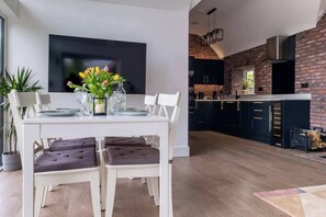 Eine moderne Küche mit Backsteinwand, einem Essbereich mit weißem Tisch und Stühlen sowie einem an der Wand befestigten Flachbildfernseher.