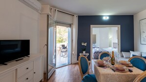 A room with a TV, a dining table set with plates, a bottle, and a chair. - GuestHost - Cozy Apartment with Terrace in Sanremo (Sanremo)