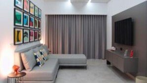 A modern living room with a grey sectional sofa, a flat-screen TV mounted on the wall, and a series of framed artworks above the sofa.