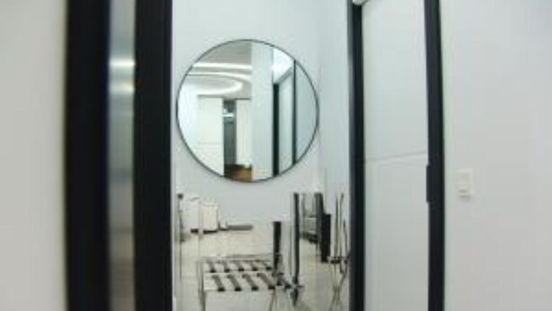 A hallway with a round mirror on the wall, a black-framed door, and a metal rack with items on it.