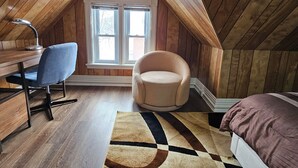 Ein gemütliches Schlafzimmer im Dachgeschoss mit Holzwänden, einem Schreibtisch mit Stuhl, einem runden Sessel, einem Bett und einem großen Teppich.