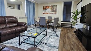 Ein Wohnzimmer mit braunem Ledersofa, einem Glastisch und einem Essbereich mit Stühlen und Tisch.