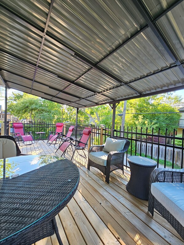 A covered outdoor deck with wicker furniture, a metal roof, and a wooden deck. - Spacious 4BR Retreat w/ King Loft Near Downtown PTBO & Hospital + Parking (Peterborough)
