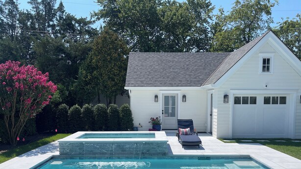A rectangular swimming pool with a stone edge, a lounge chair, and a potted plant near a white house with a garage. - Family Beach House 4 blocks from Beach (Sea Girt)